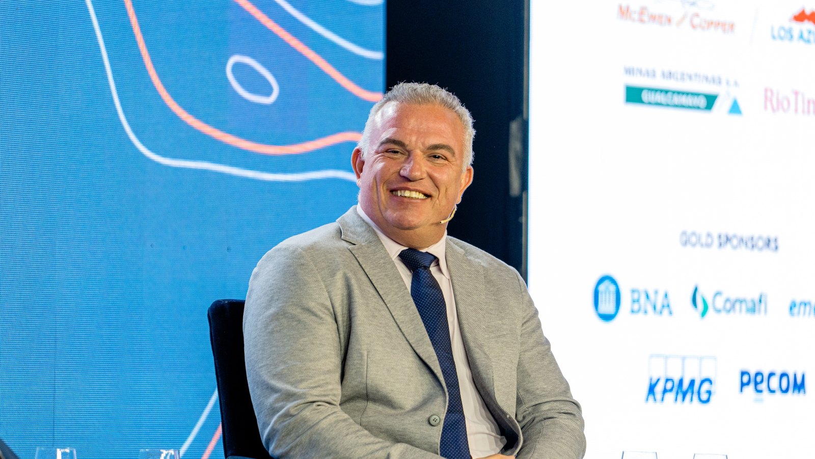 Michael Meding on stage at the Forbes Mining Summit, with the McEwen Copper and Los Azules logos on the sponsor wall